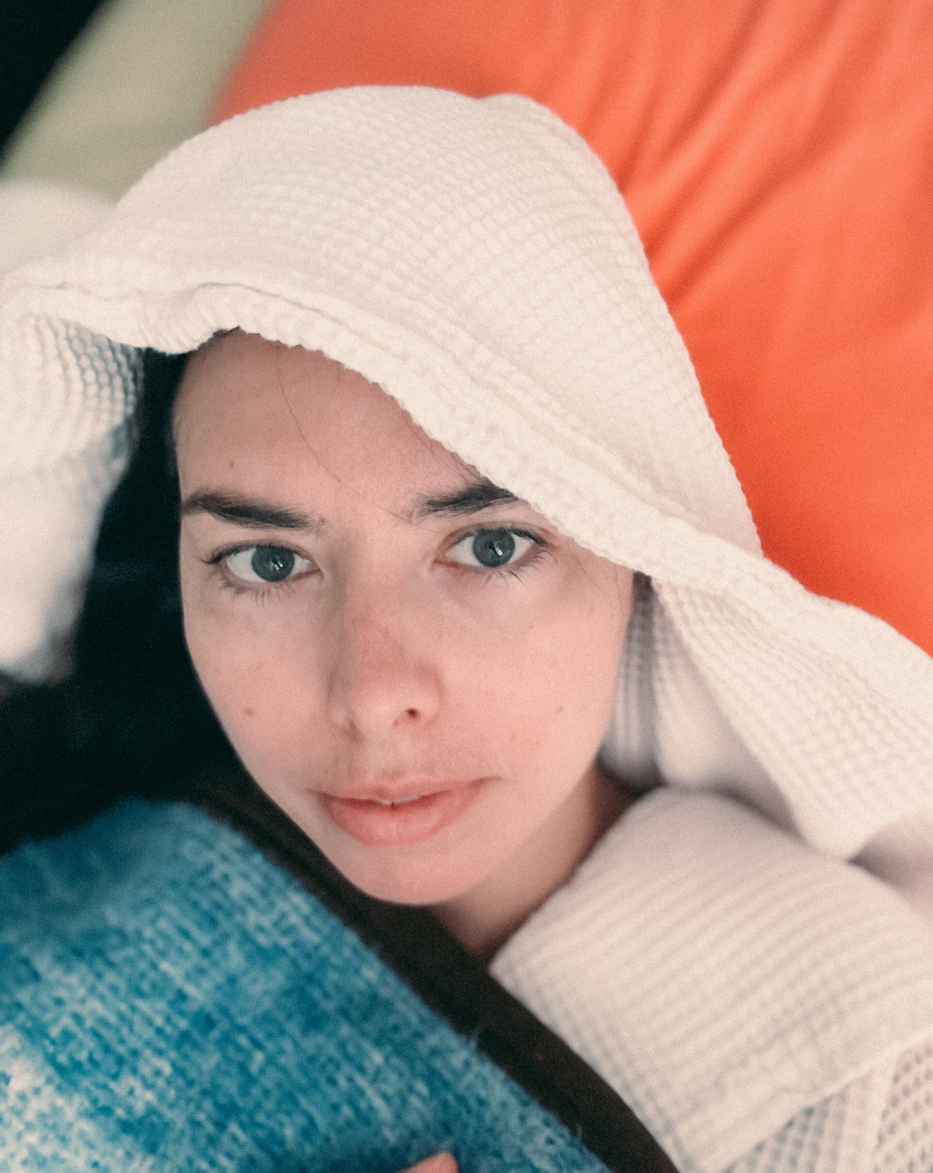 A high-masking, late-diagnosed autistic woman in autistic burnout, a young woman in bed under a blanket, wearing a white bathrobe with a hood