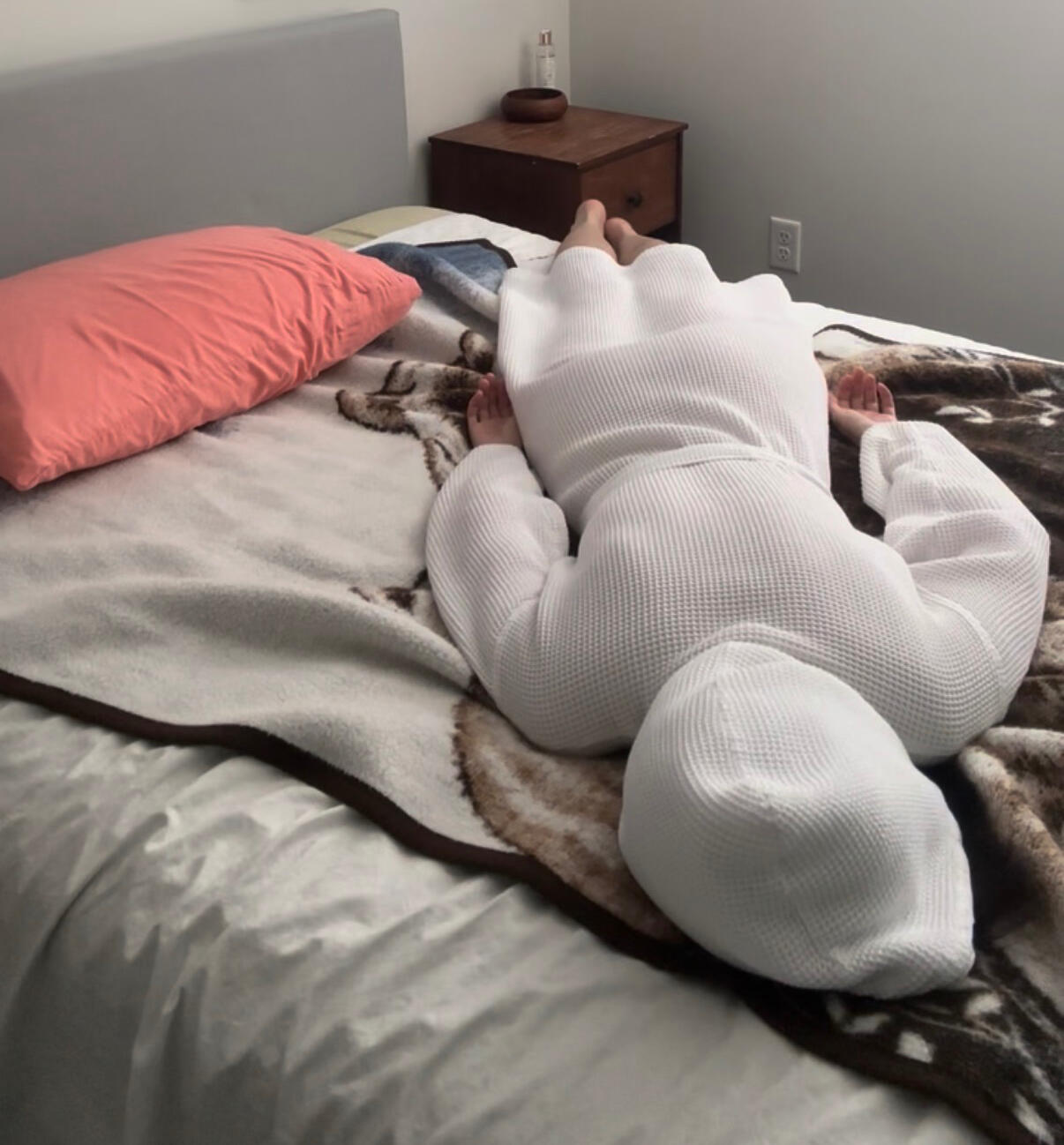 An exhausted woman lies face down on a bed, on top of a fuzzy blanket, wearing a white bathrobe.
